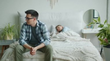 Karısı evde uyurken üzgün yüzüne dokunarak yatakta oturan endişeli adam