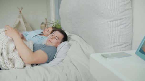 Somnolent homme se réveillant en regardant smartphone souriant puis sieste avec sa femme au lit — Video