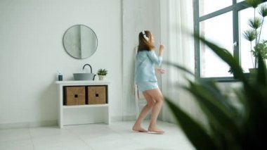 Banca dans eden pijamalı neşeli kadın diş fırçası ile eğlenerek şarkı söylüyor