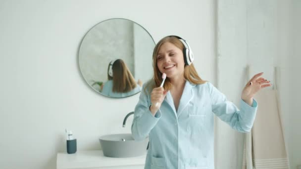 Estudiante feliz cantando en cepillo de dientes bailando disfrutando de la música en auriculares en casa — Vídeos de Stock