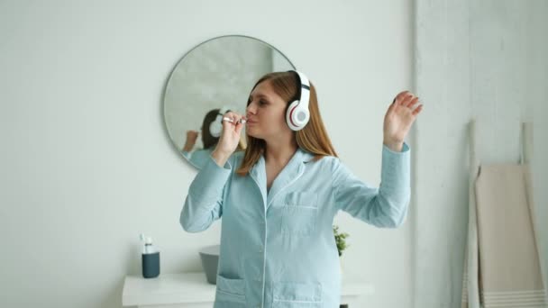 Movimiento lento de la mujer feliz en los auriculares cepillarse los dientes bailando en el baño — Vídeos de Stock