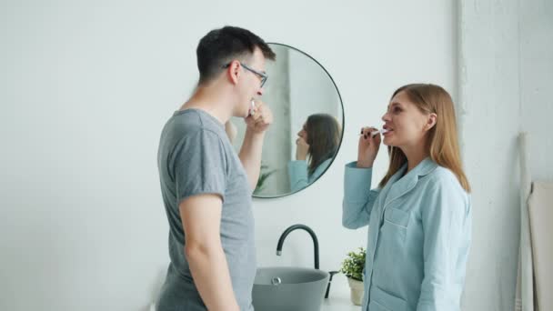Hombre y mujer en pijama cepillándose los dientes hablando sonriendo en apartamento moderno — Vídeo de stock