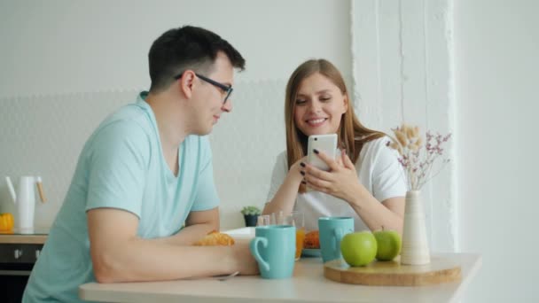 Powolny ruch mężczyzny i kobiety przy użyciu smartfona przy stole w kuchni na śniadanie — Wideo stockowe