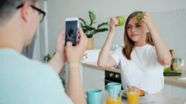 Kocası mutfakta akıllı telefon ile fotoğraf çekerken elma ile poz eşi