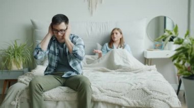 Kızgın karısı evde bağırırken üzgün yüzüne dokunarak yatakta oturan mutsuz adam