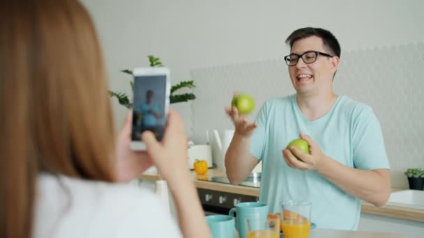 Медленное движение мужчины, жонглирующего яблоками, пока женщина фотографируется со смартфоном — стоковое видео