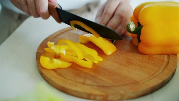 Mano femenina rebanando pimiento amarillo con cuchillo en tabla de madera haciendo ensalada vegana — Vídeo de stock