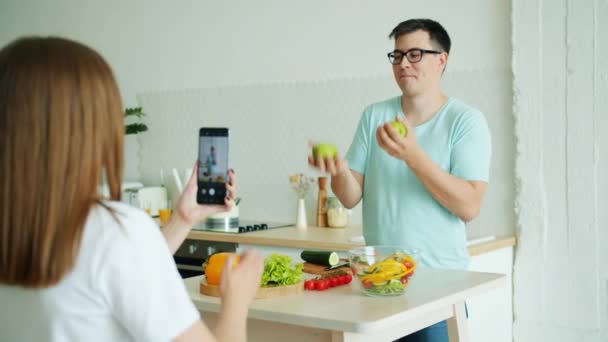 女性が写真を撮っている間、男はリンゴをジャグリングし、その後、スマートフォンのカメラのためにポーズ — ストック動画