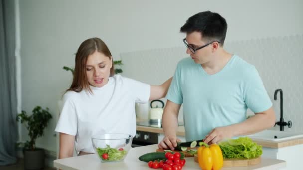 Hombre cocina ensalada corte pepino alimentación novia besos en cocina en casa — Vídeos de Stock