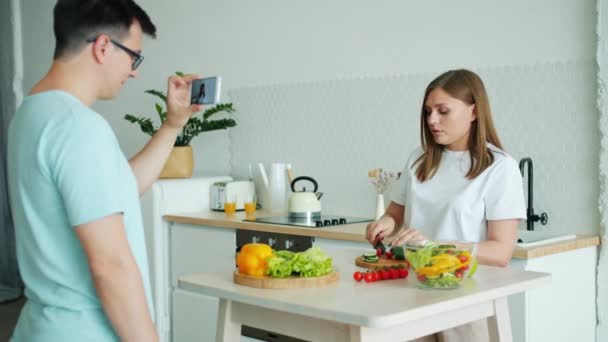 Mädchen beim Salatkochen reden und Daumen hoch zeigen, während Kerl Video für Vlog aufnimmt — Stockvideo