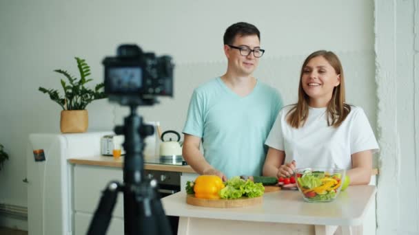 Menina e cara gravação de vídeo sobre comida orgânica com câmera na cozinha em casa — Vídeo de Stock