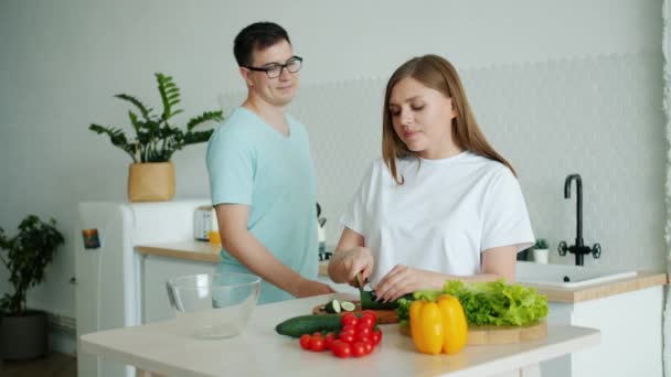 Slow Motion van vrouw koken salade in keuken dan voeden echtgenoot met komkommer — Stockvideo