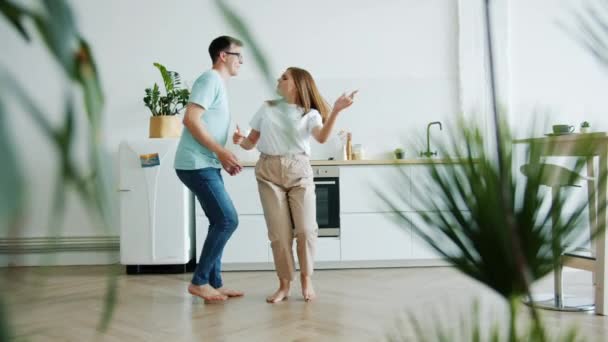 Movimento lento do jovem casal dançando na cozinha em casa de mãos dadas se divertindo — Vídeo de Stock