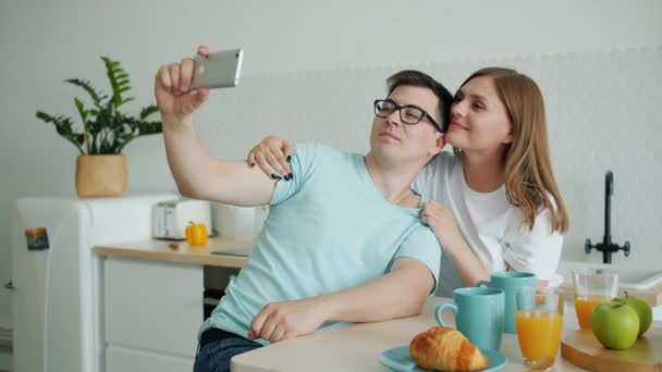 Pareja feliz besando y tomando selfie con smartphone en la cocina en casa — Vídeos de Stock