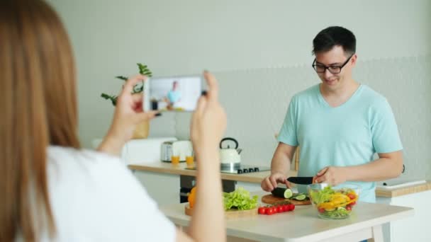 Un par de vloggers grabando video de un chico cocinando ensalada en la cocina en casa — Vídeos de Stock