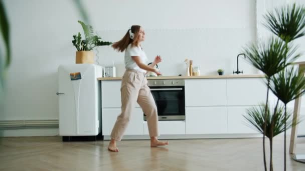 Mouvement lent de l'étudiant heureux dansant dans la cuisine portant des écouteurs s'amusant — Video