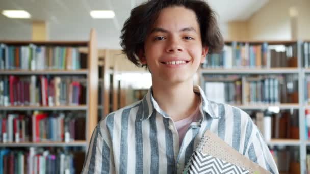 Retrato em câmera lenta de adolescente alegre em pé na biblioteca da escola com livros — Vídeo de Stock