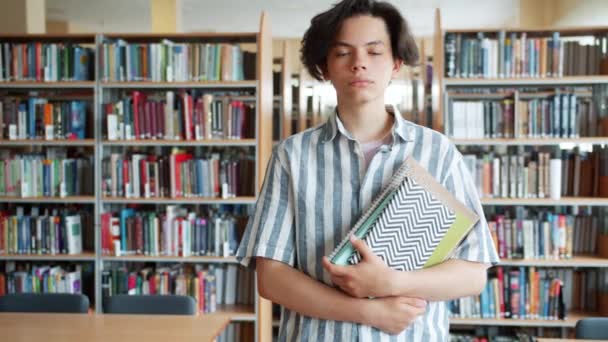 Retrato en cámara lenta de un estudiante adolescente serio parado en la biblioteca con libros — Vídeos de Stock