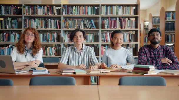 Портрет молодих студентів, які сидять у бібліотеці, посміхаючись дивитися на камеру — стокове відео