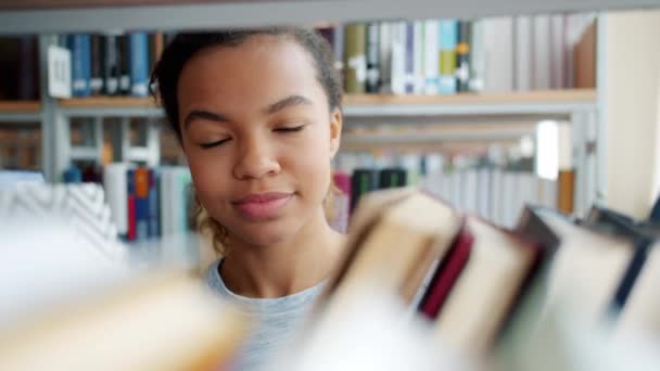 Портрет жизнерадостного афроамериканского подростка, выбирающего книги в школьной библиотеке — стоковое видео