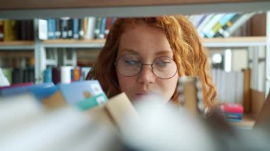 Kitapçıda kitap seçen genç bayan kapalı mekanlarda gülümseyerek kitap okuyor