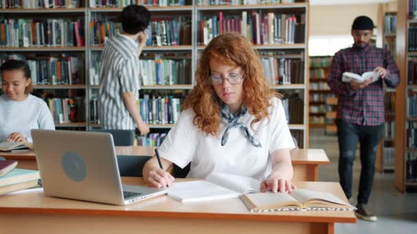 使用书籍和笔记本电脑写作阅读在图书馆学习的人的慢动作 — 图库视频影像