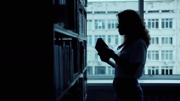 Silhouette einer klugen Frau, die ein Buch in der Bibliothek liest und es in Händen hält — Stockvideo