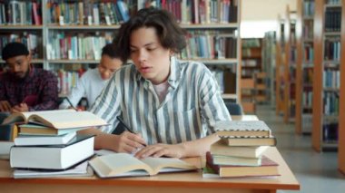 Üniversite kütüphanesinde okuyan yorgun çocuğun yavaş hareketi masada kitap okuyor