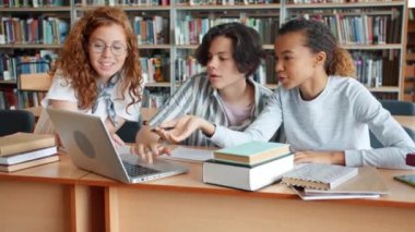 Öğrenciler kız ve adam dizüstü bilgisayar ve kitap kullanarak kütüphanede projede çalışan