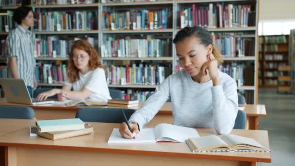 Kütüphanede çalışan bir grup öğrenci kapalı alanda ders yazma kitaplarını okuyor — Stok video