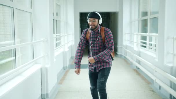 Bonito afro-americano cara em fones de ouvido dançando no corredor da universidade se divertindo — Vídeo de Stock