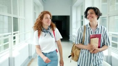 Lise salonunda yürüyen kız ve erkek öğrenciler arkadaşlarına kitap vererek konuşuyor