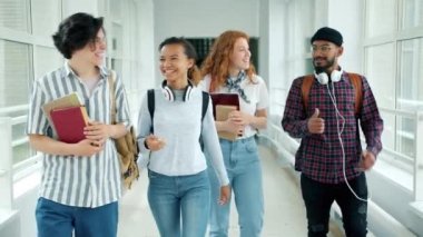 Neşeli öğrenciler üniversite salonunda başparmak-up gösteren kitaplarla yürüyüş konuşuyor