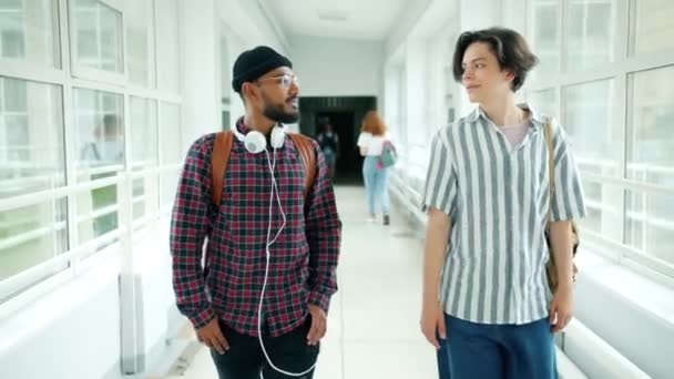 Mužští studenti chodící v univerzitní hale s batohy v rozhovoru po vyučování — Stock video