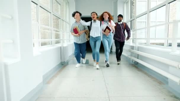 Dolly shot de jeunes heureux courir dans le couloir de l'université tenant des livres rire — Video