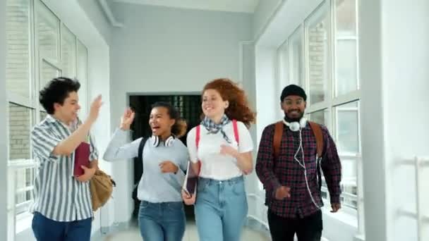 Felices amigos corriendo en el pasillo de la escuela haciendo chocar los cinco saltos de risa — Vídeos de Stock