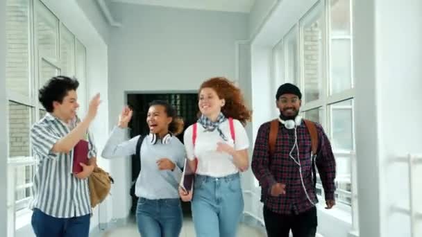 Amigos felizes correndo no corredor da escola fazendo high-five risos pulando — Vídeo de Stock