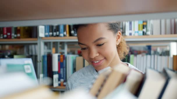 Hermosa chica adolescente afroamericana eligiendo libros en la biblioteca universitaria — Vídeos de Stock