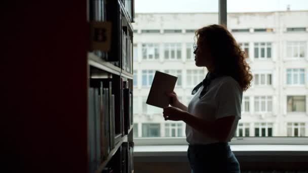 Lento movimiento de estudiante sonriente eligiendo libro en lectura de biblioteca escolar — Vídeos de Stock