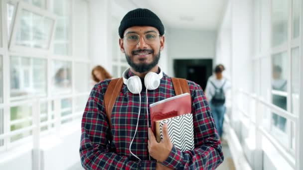 Retrato de jovem estudante segurando livros em pé na sala da universidade sorrindo — Vídeo de Stock