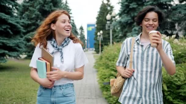 Casal de adolescentes andando ao ar livre falando segurando livros bebendo café — Vídeo de Stock