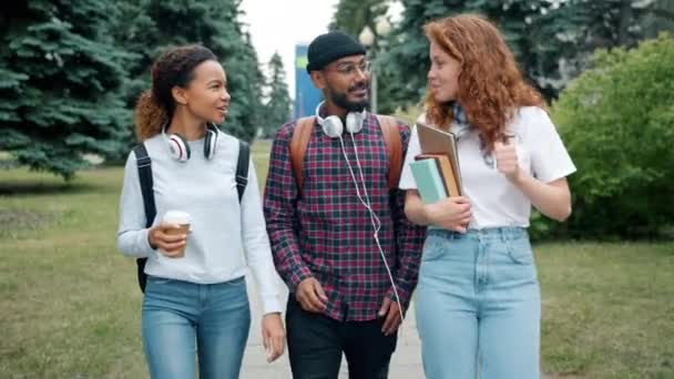 Zeitlupe von Männern und Frauen, die draußen auf dem Campus mit Büchern und Kaffee spazieren gehen — Stockvideo