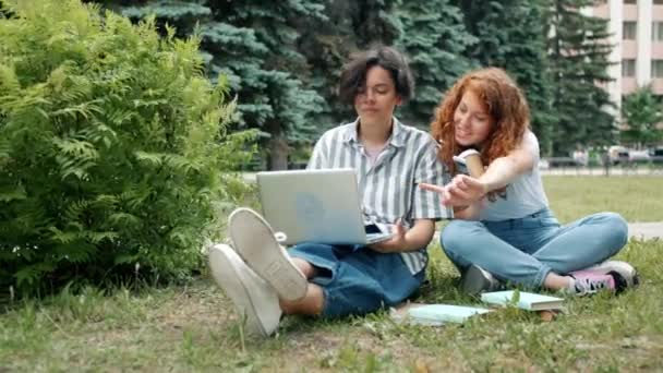 Paar studenten studeren buitenshuis met behulp van laptop lezen boeken praten — Stockvideo