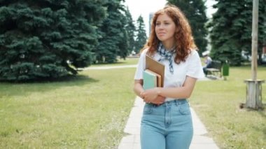 Pretty redhead bayan öğrenci sonbaharda gülümseyerek kitap tutan parkta yürüyüş