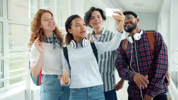Estudantes alegres fazendo videochamada on-line com smartphone no salão da faculdade — Vídeo de Stock