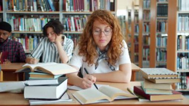 Kütüphanede okuyan yorgun kızıl saçlı kız sonra kapalı rahatlatıcı masada uyuyor