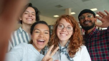 Üniversite kütüphanesinde selfie çeken çok ırklı bir grup genç gülümsüyor.