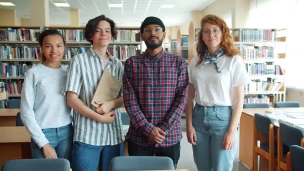 Zeitlupenporträt fröhlicher Studenten, die in der Bibliothek stehen und Bücher in der Hand halten — Stockvideo