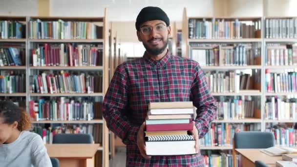 Movimento lento de estudante afro-americano bonito andando na biblioteca com livros — Vídeo de Stock