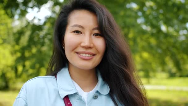 Mooie Aziatische vrouw staande buitenshuis in Park glimlachend kijken naar camera — Stockvideo